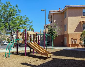A playground with a slide and a tree in front of a building.
